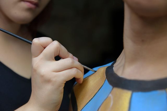 Una mano sujeta el pincel mientras termina el borde negro de un collar pintado en la piel