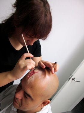 Una maquilladora dibuja con un palillo una herida en la cabeza rapada de un hombre