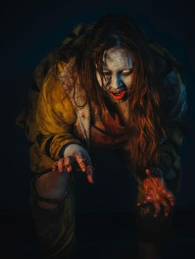 Zombi agazapado en la oscuridad, que avanza con las manos ensangrentadas por delante y la boca roja entreabierta