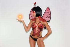 Torso pintado de rojo como una mariquita, con alas de tela y una luz en la mano
