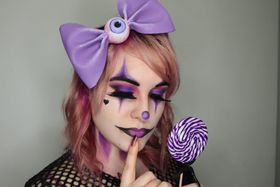 Párpados cerrados con sombra morada y rosa bajo unos rombos lila, y un dedo apoyado en los labios morados