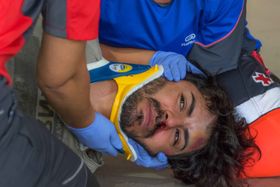 Primer plano de un herido con collarín amarillo, moratones y sangre bajo la nariz