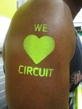 Gran corazón amarillo flúor estarcido en la parte alta de un brazo, con letras encima y debajo