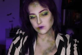 Cara blanquecina con manchas de moho verde en la barbilla y el cuello, sombra verde y dorada en los párpados y labios morados, sobre una chaqueta de rayas blancas y negras