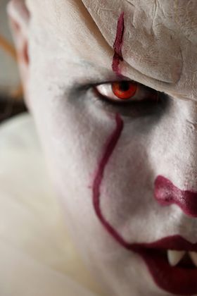 Primer plano de un payaso de cara blanca con un ojo rojo y una línea granate que le cruza la mejilla hasta la boca