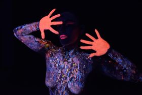 Torso cubierto de salpicaduras que brillan bajo luz ultravioleta, con las palmas de las manos pintadas de naranja