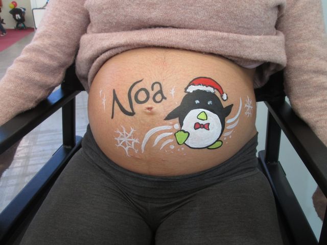 Pingüino con gorro de Papá Noel y pajarita roja pintado sobre la barriga, entre copos de nieve y junto a un nombre en letras negras
