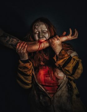 Zombi de piel gris y agrietada y ojos en blanco que muerde un antebrazo; la sangre le corre por el brazo