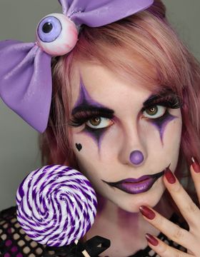 Cara de payaso en tonos lila: rombos morados en los ojos, nariz de bola, labios morados perfilados en negro y un corazón negro en la mejilla; en la cabeza, un lazo lila con un ojo de juguete