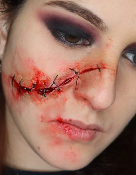 Corte cosido con puntos negros que cruza la mejilla y la nariz, con los ojos maquillados en tonos ahumados